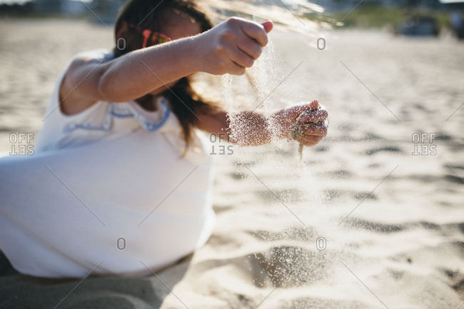 Girl letting sand fall through her fingers at the beach