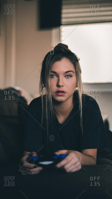 Attractive young woman with blue eyes and rings in ears lying with blue joystick and looking at camera