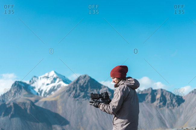 Side view of  bearded male in hat holding camera with professional lens and looking away in Iceland