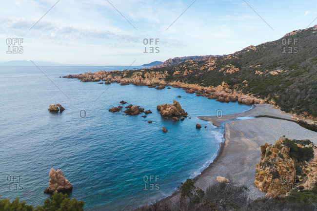 View to coastal hill and rocks and blue ocean in daylight.