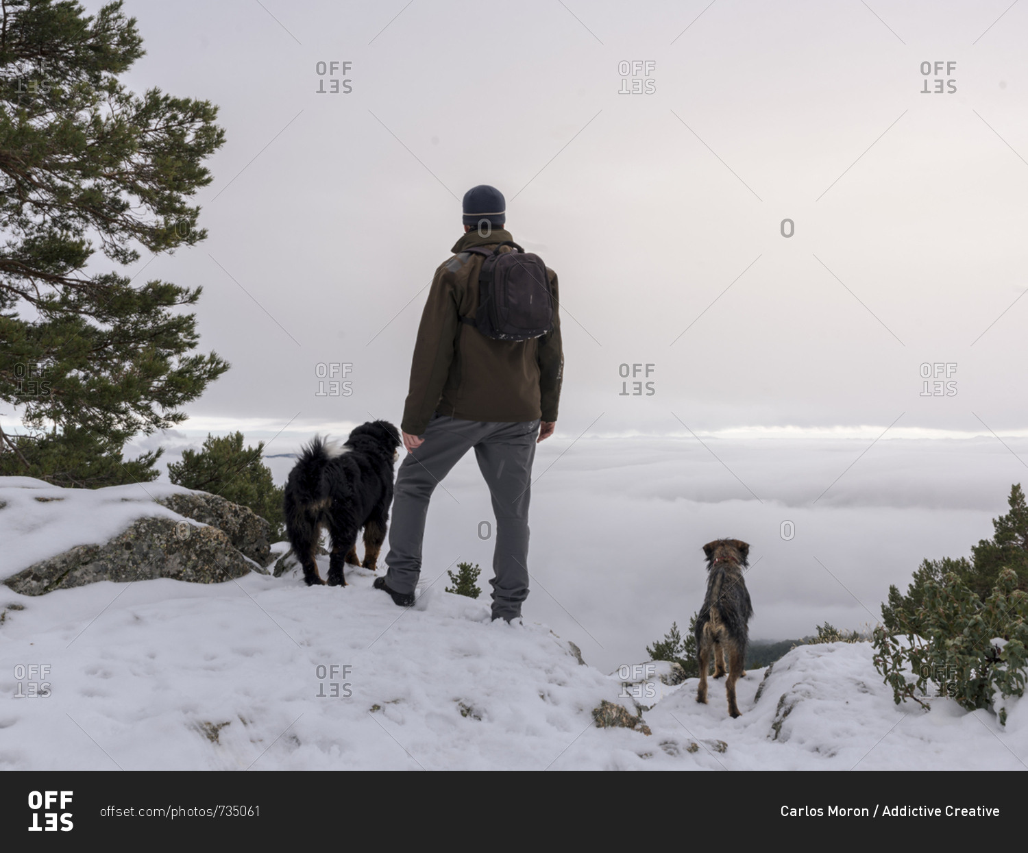 Hiker and his dog looking in the snowy mountains at foggy sky background.