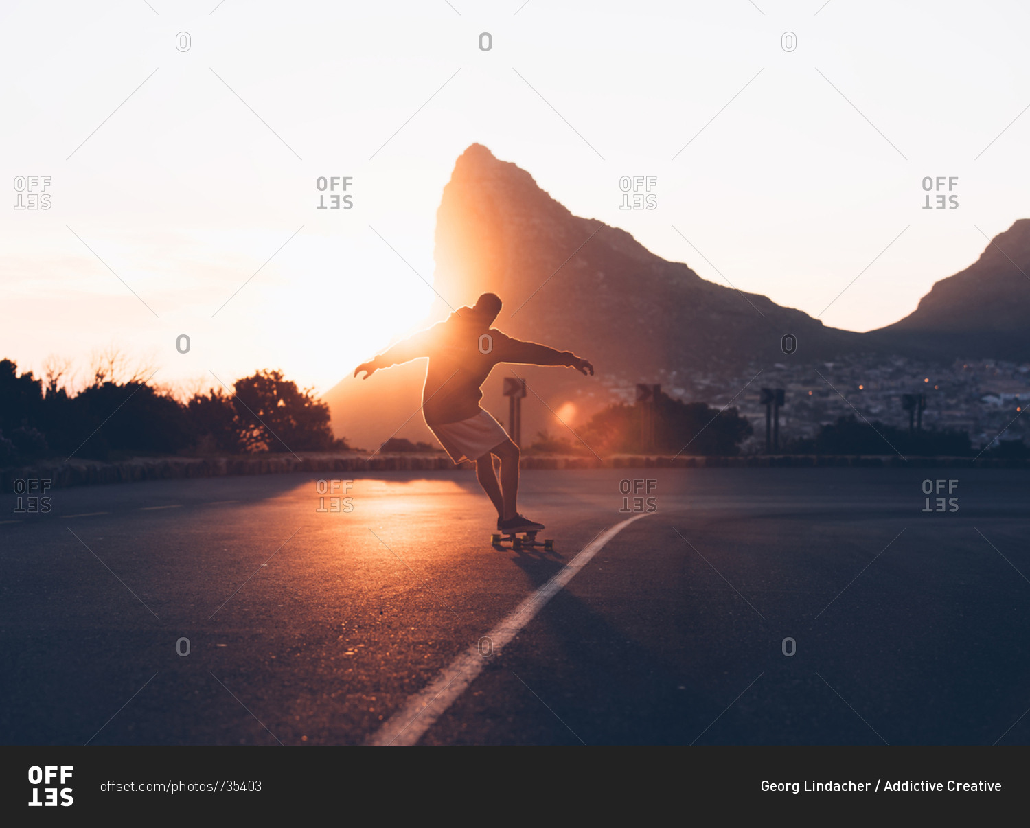 Back view of man riding on skateboard on asphalt road down the hill in backlit.
