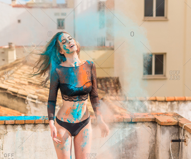Skinny sexual woman in black lingerie all covered with colorful dry powders and standing on stone balcony