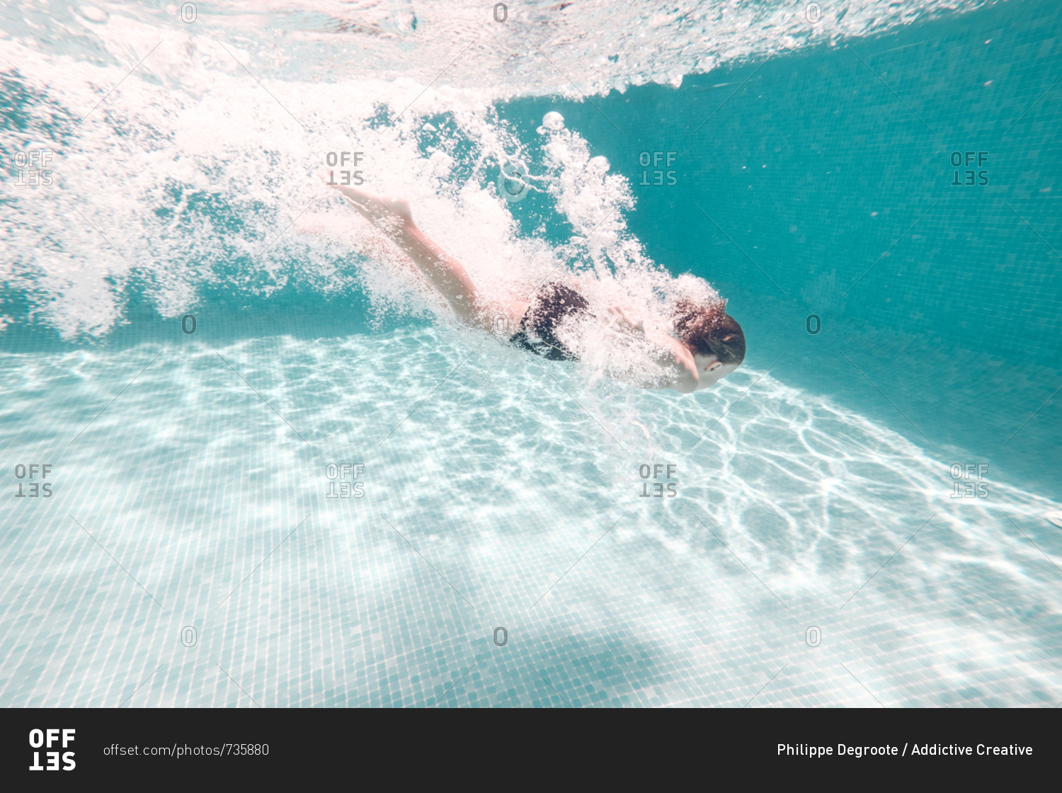 Unrecognizable boy in swimming trunks dives into transparent blue pool water.