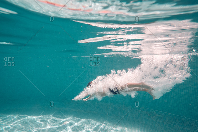 Unrecognizable boy in swimming trunks dives into transparent blue pool water.