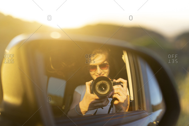 Young woman taking picture of her mirror image in her car