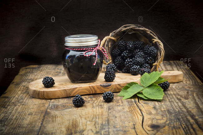 Glass of homemade blackberry jelly and blackberries on wood