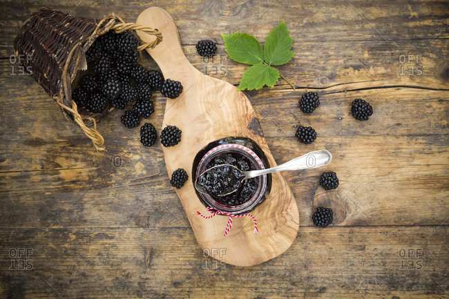 Glass of blackberry jelly and blackberries on wood