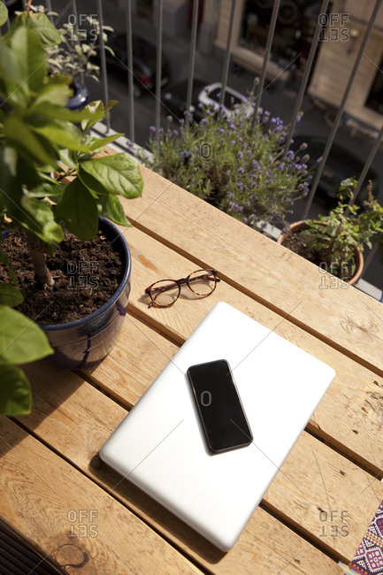 Smartphone- laptop and spectacles on palette on balcony