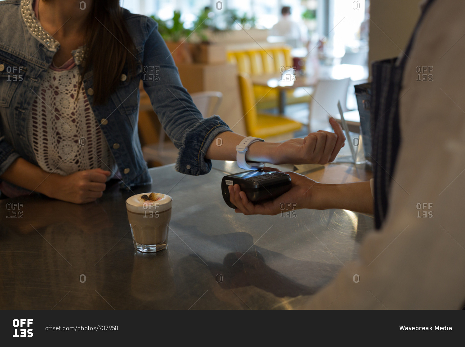 Mid section of woman paying with NFC technology on smartwatch in cafe