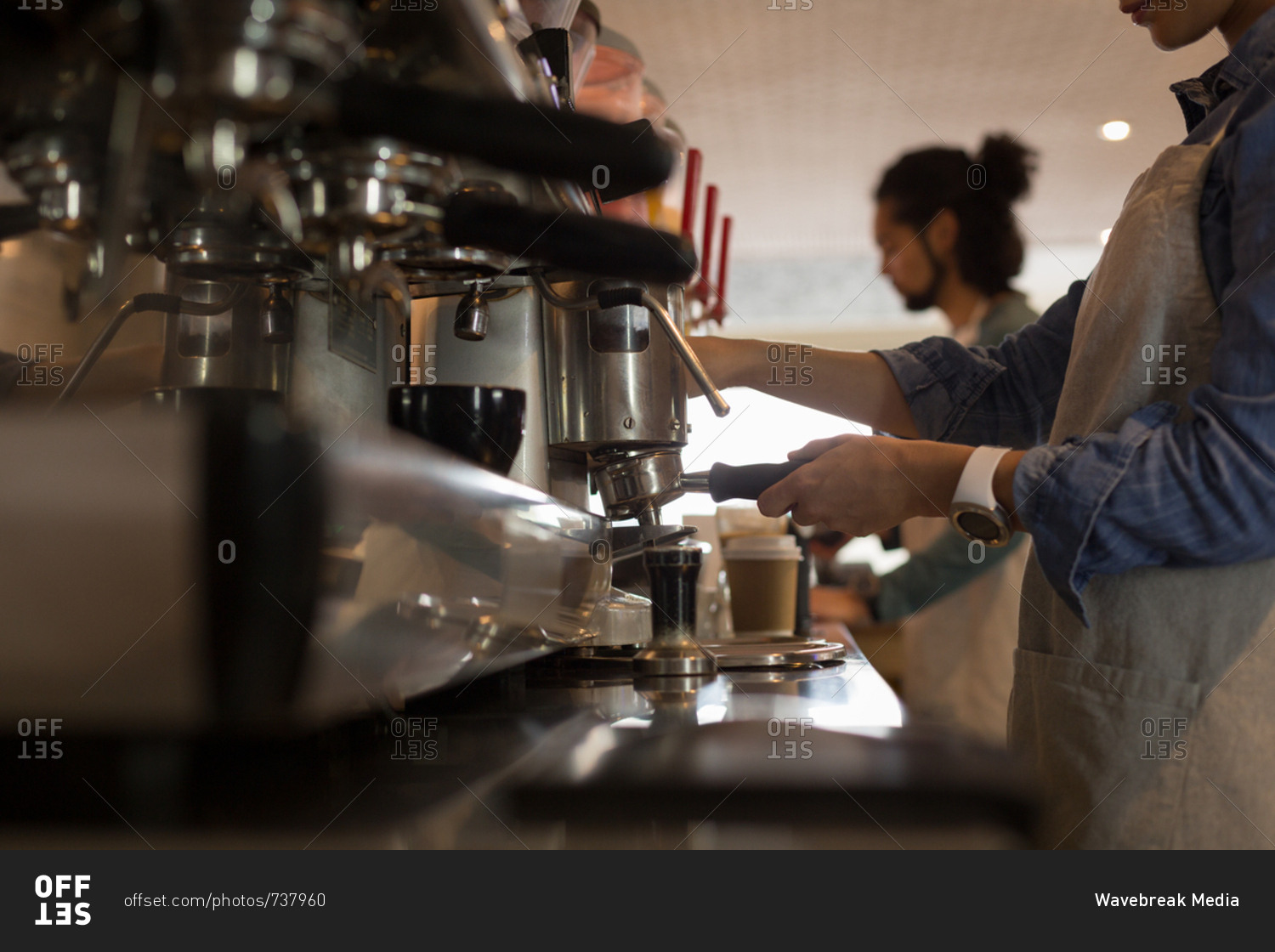 Mid section of waitress preparing coffee at coffee machine in cafe