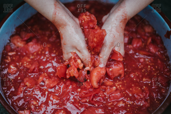 Close-up of a hands squeezing chopped tomatoes in a bowl
