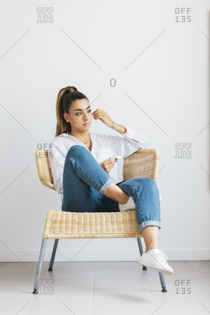 Young Woman Relaxing In Chair And Putting On Wireless Earbuds Stock Young Woman Relaxing In Chair And Putting On Wireless Earbuds Stock Photo Offset