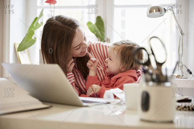 Smiling woman talking to daughter while working on laptop at home