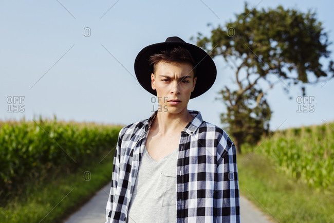 Handsome country boy with hat posing on the country road near to a cornfield
