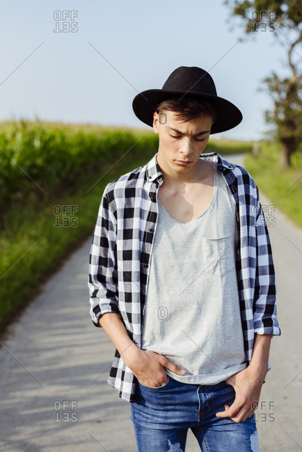 Handsome country boy with hat posing on the country road near to a cornfield