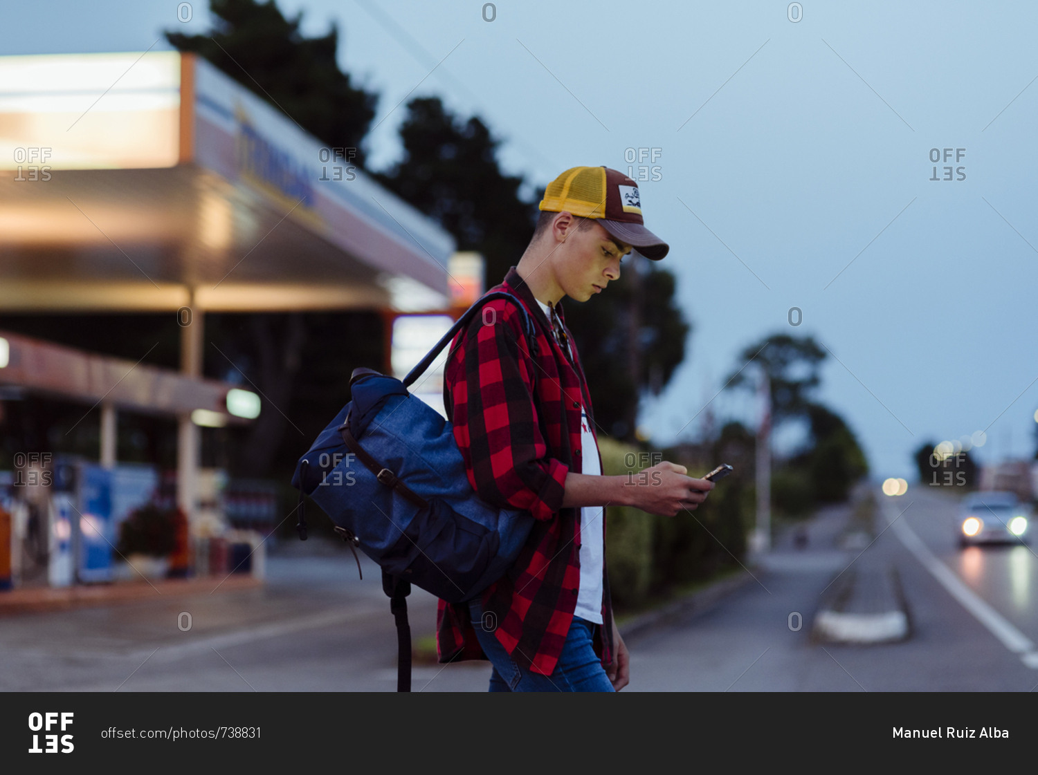 Handsome country boy with trucker cap and backpack using phone on the gas station