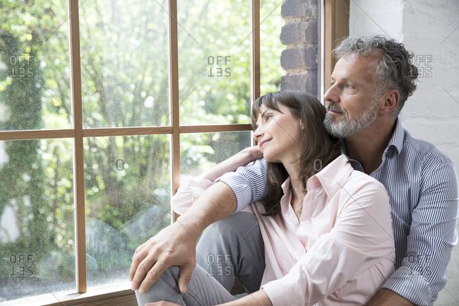 Mature couple sitting on window sill- looking out of window