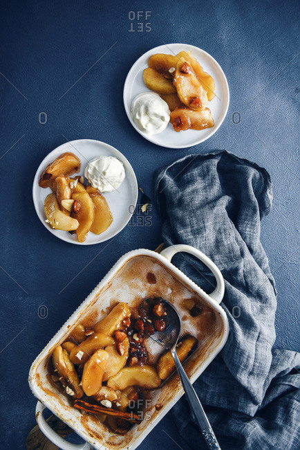 Cinnamon baked apple slices in a baking pan accompanied by two white plates with baked apple slices.