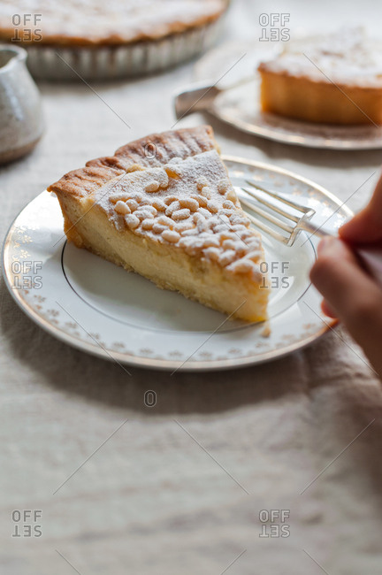 Hand eating a slice of custard pie with pine nuts