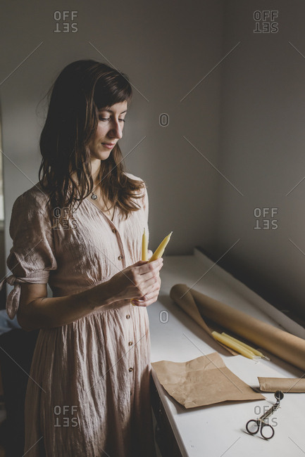 A brunette woman looks down at two beeswax pillar candles that she crafted