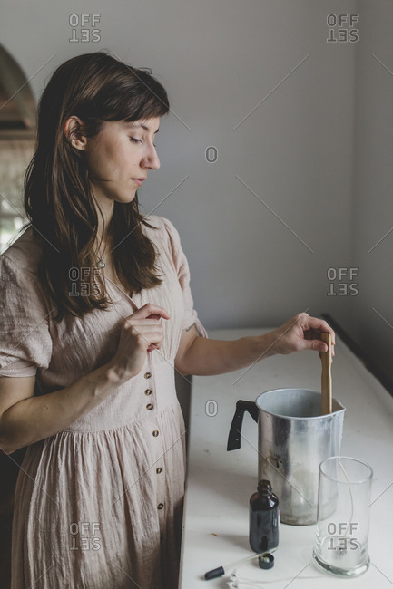 A brunette woman stirring essential oil scent to her wax for the candle she is making