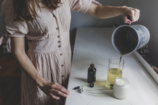 Brunette woman pouring her wax into the glass jar of the candle she is making