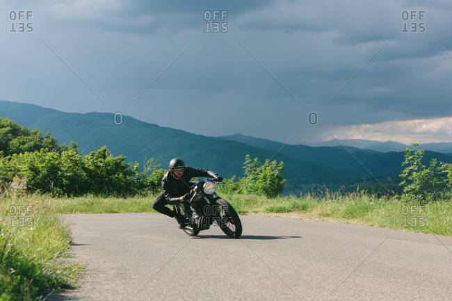 Young male motorcyclist on vintage motorcycle swerving around rural road bend, Florence, Tuscany, Italy