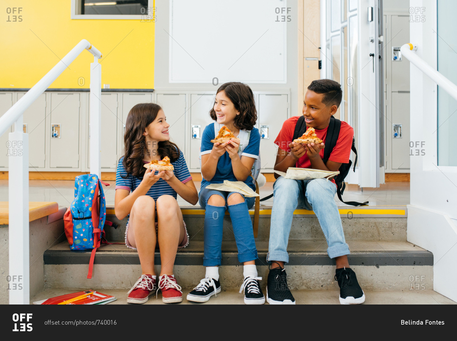 Smiling children sitting on steps looking at each other and eating lunch together at school