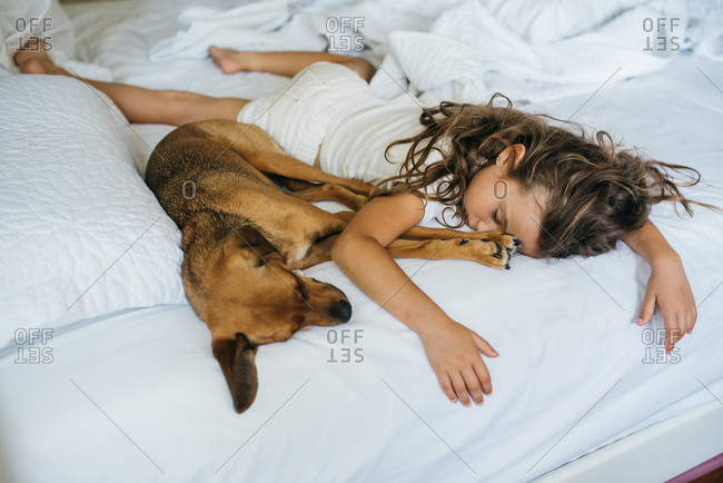 Girl sprawled out on bed sleeping with her pet dog