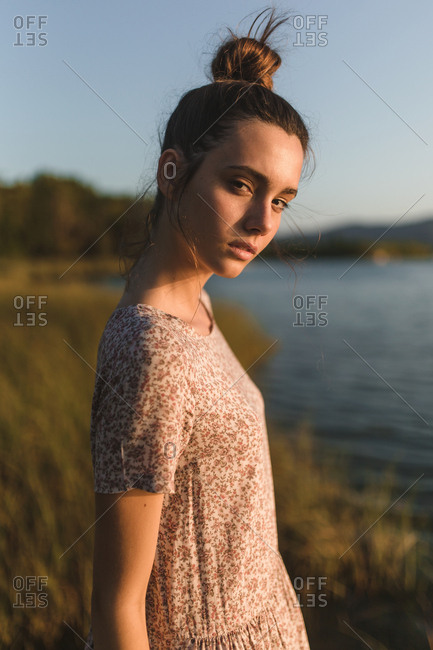 Portrait of young brunette girl with a hair bun observing and relaxing in a lake in a sunset of summer