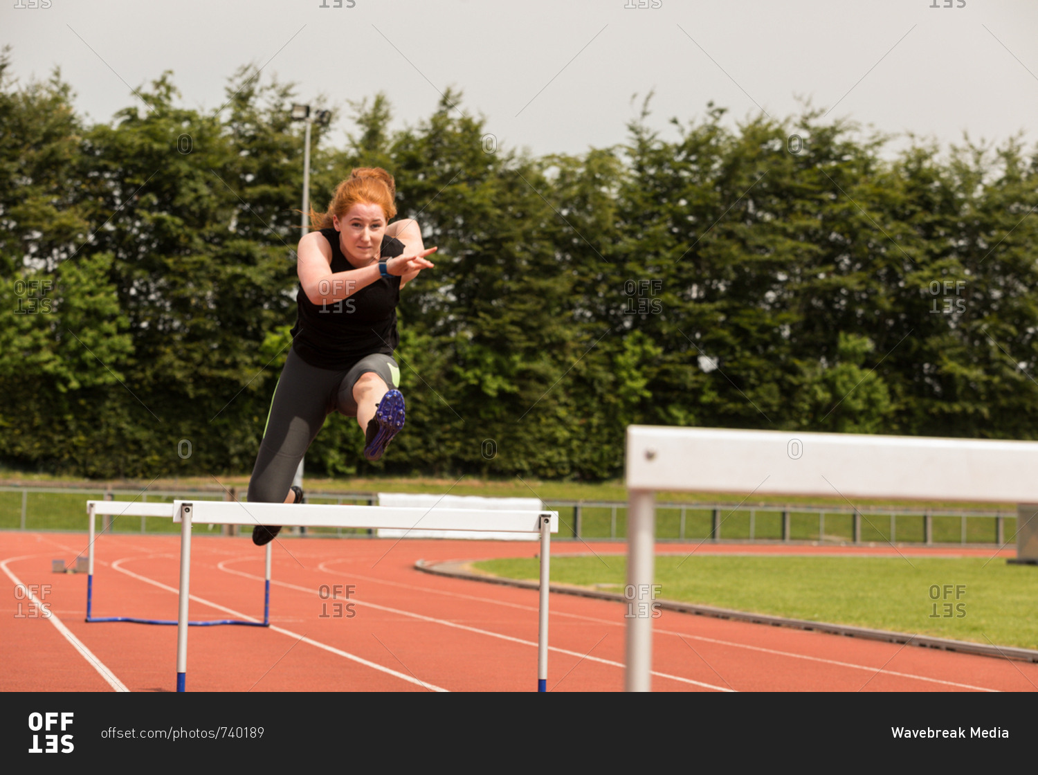 Female athletic jumping over hurdle on sports track