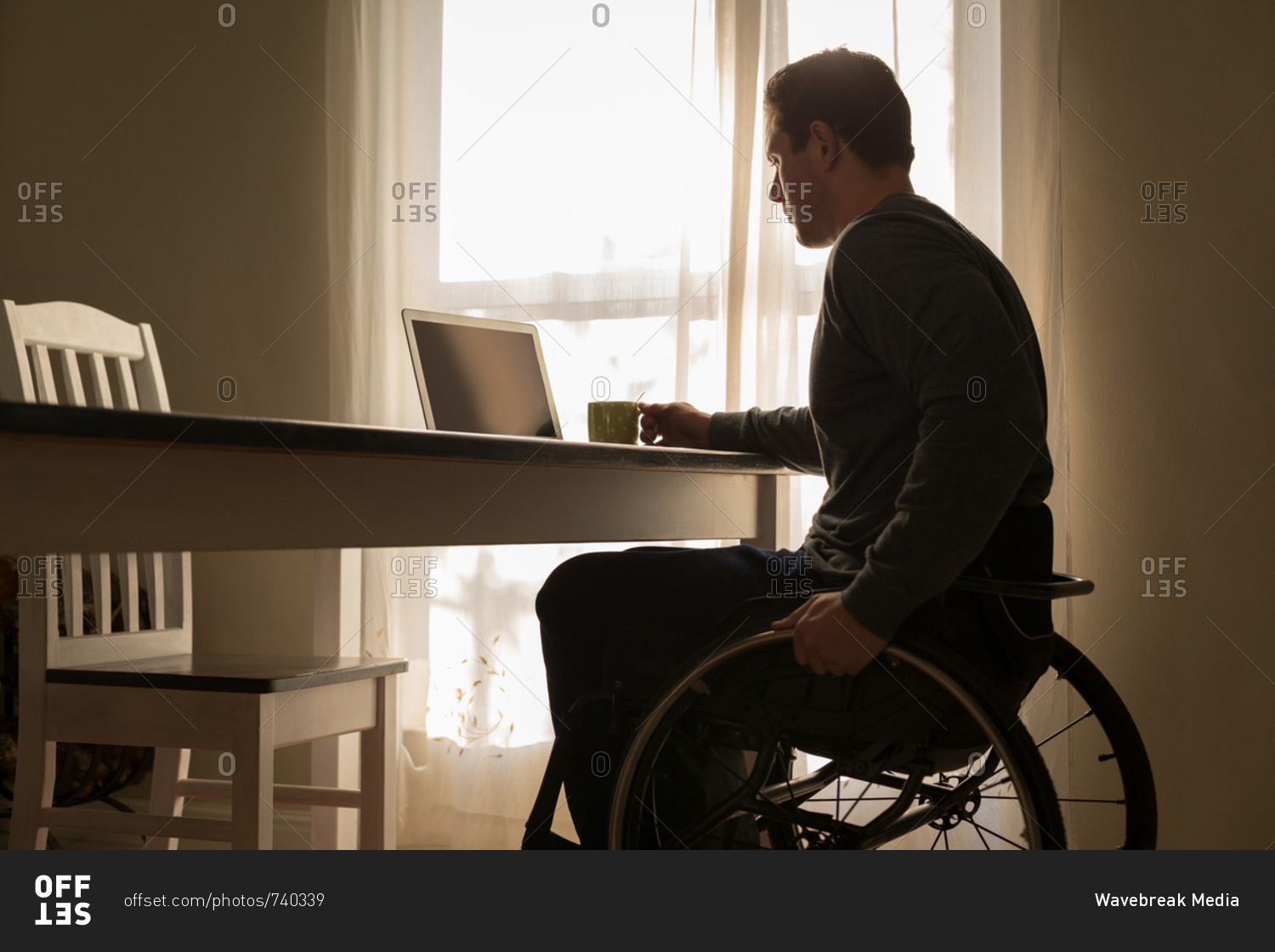 Disabled man having coffee while using laptop on dinning table at home