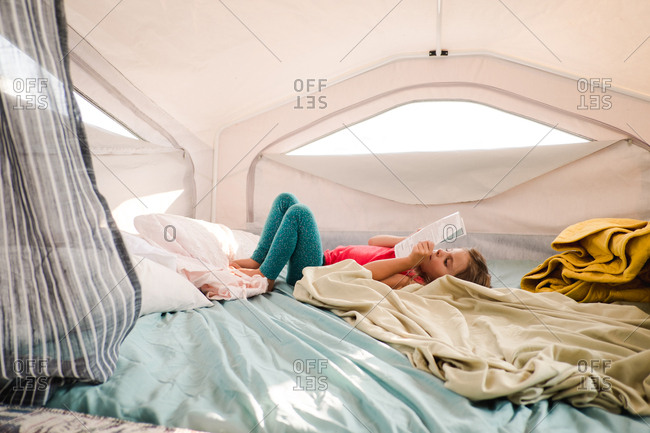 Girl lying on bed and reading inside tent