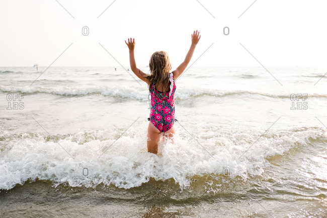 Girl with arms up standing in the ocean as waves splash around her