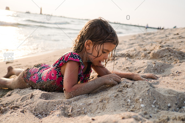 Girl covered in wet sand lying on the beach