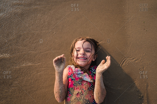 Smiling girl covered in wet sand lying on the beach