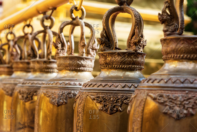Ancient decorative bells with metal design hanging in temple in sunlight, Chiang Mai