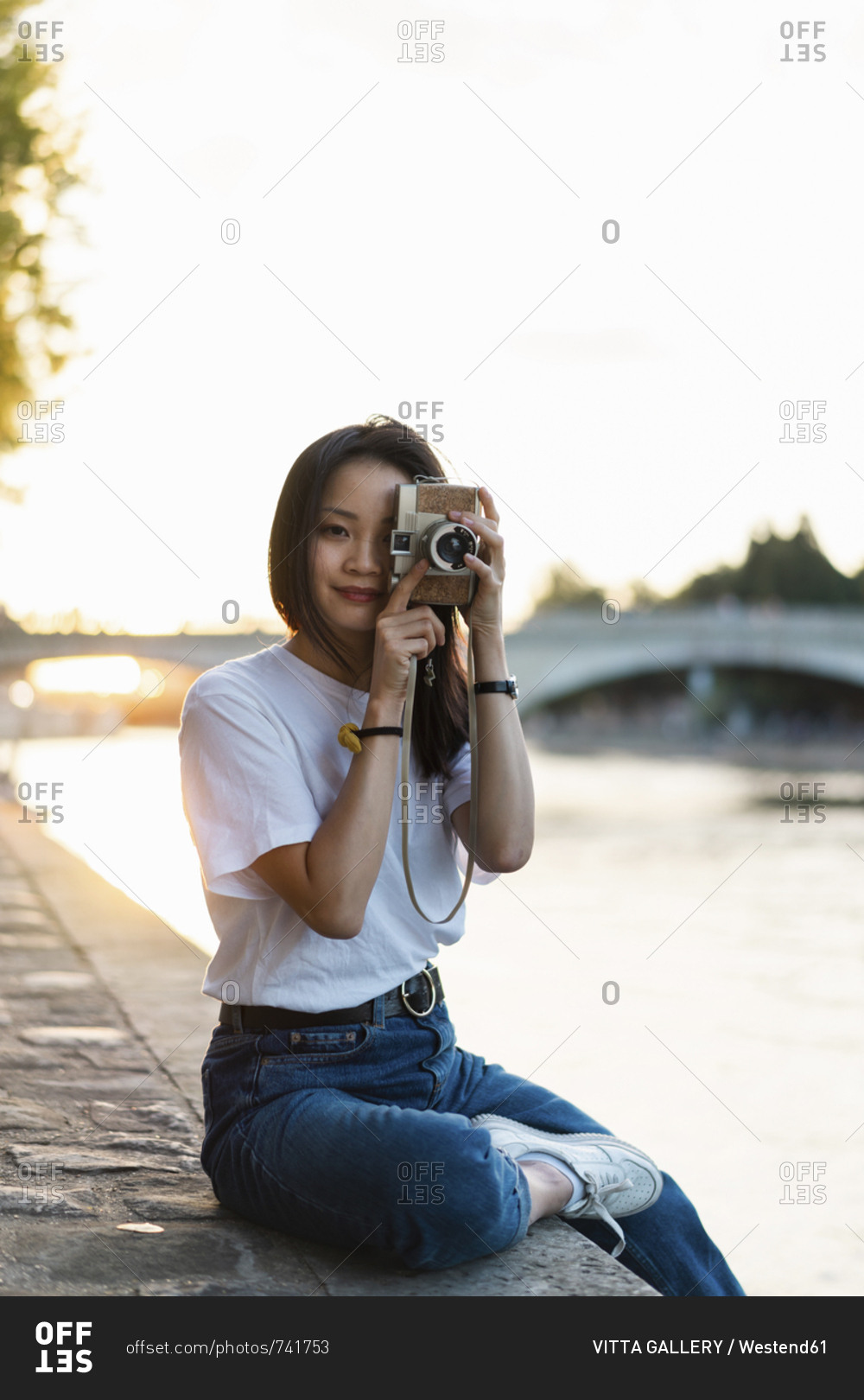 France- Paris- portrait of young woman with camera at river Seine at sunset