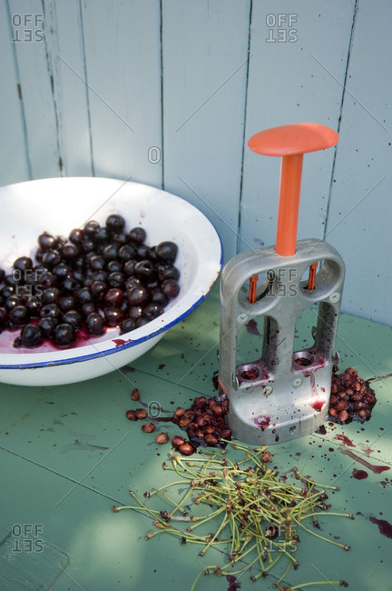 Bowl of pitted cherries- pit remover- pits and stems