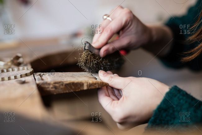 Crop close up hands of woman carving and brushing little detail with brush at desk