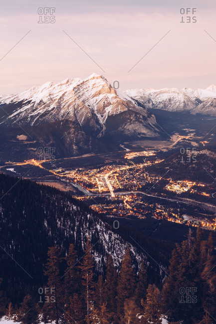 View from height of snowy mountain range with glowing city far away in valley below