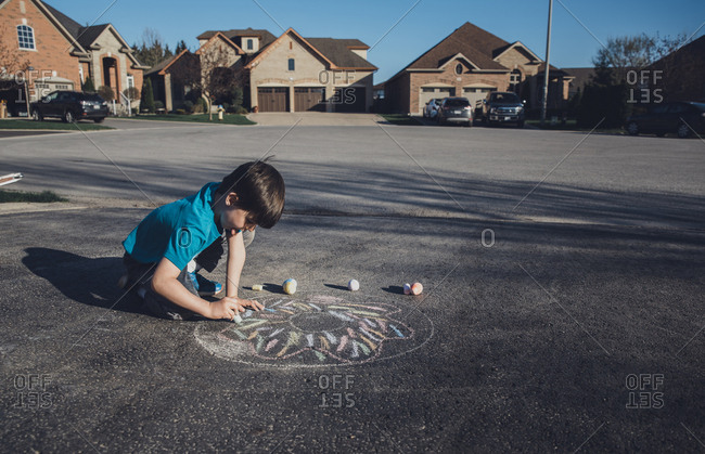 Side view of boy drawing with chalk on asphalt against houses