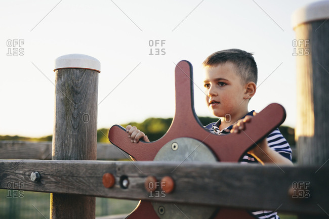 Boy looking away while playing with outdoor play equipment against clear sky during sunset