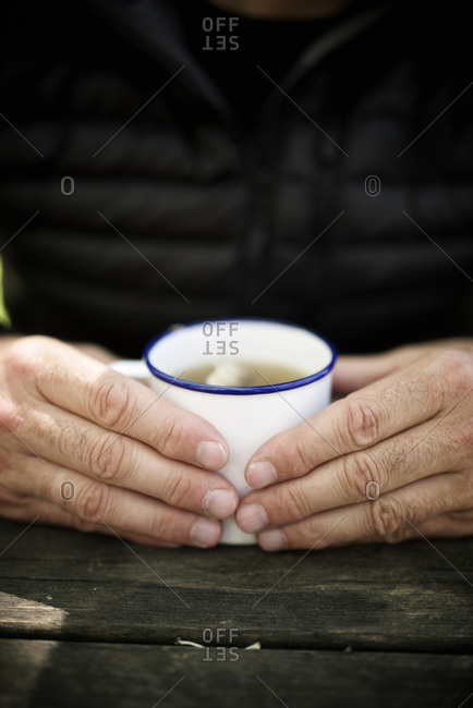 Midsection of man holding tea in cup on wooden table