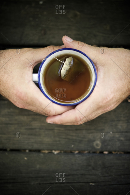 Cropped hands of man holding teabag in cup on wooden table