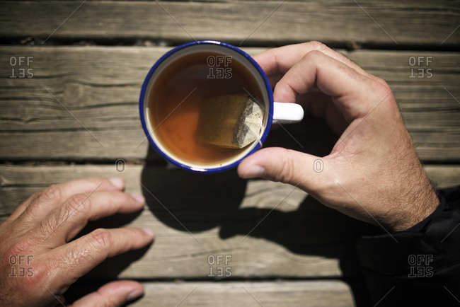 Cropped hands of man holding tea in cup on wooden table