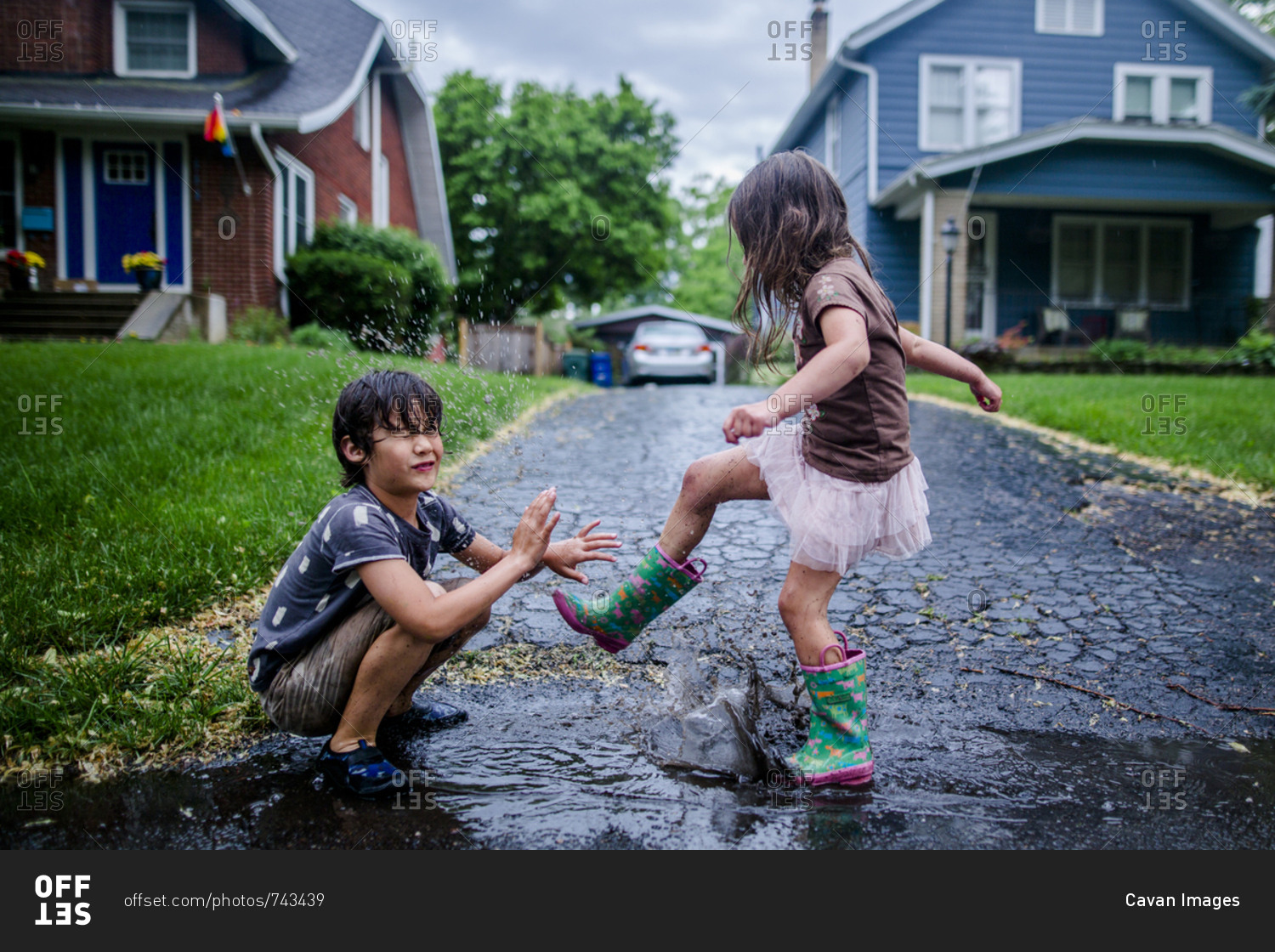 Side view of playful sister splashing puddle on brother during rainy season
