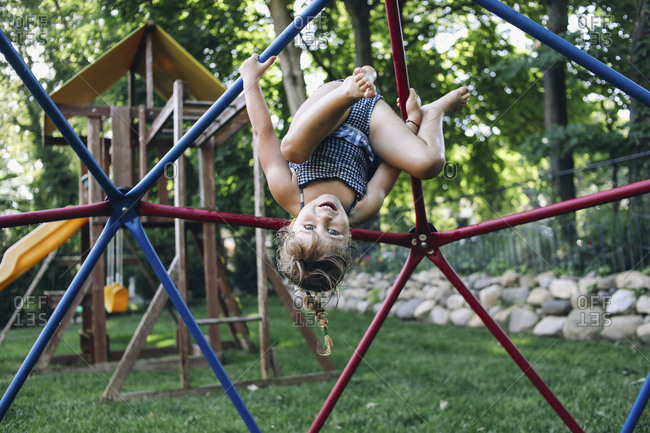 Portrait of cute smiling girl hanging upside down on jungle gym against trees at playground