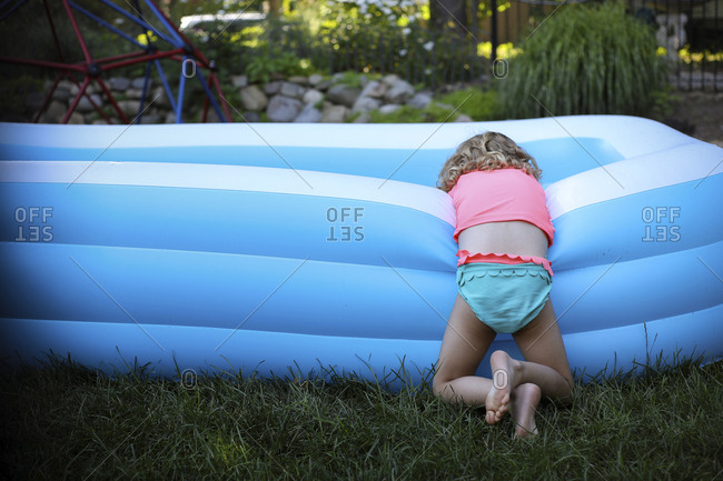 Rear view of girl leaning on blue wading pool at backyard